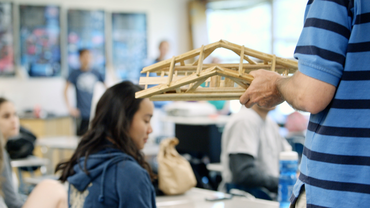 Student holds a bridge made out of popsicle sticks