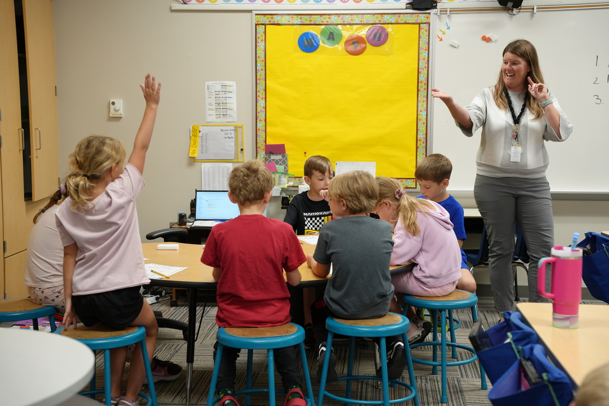 a teacher smiles and points to a student with their hand raised