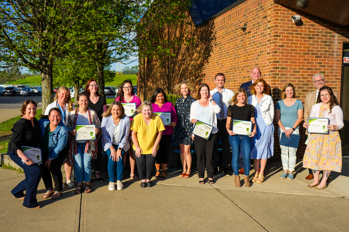 Volunteers and principals pose for a photo in front of a school.