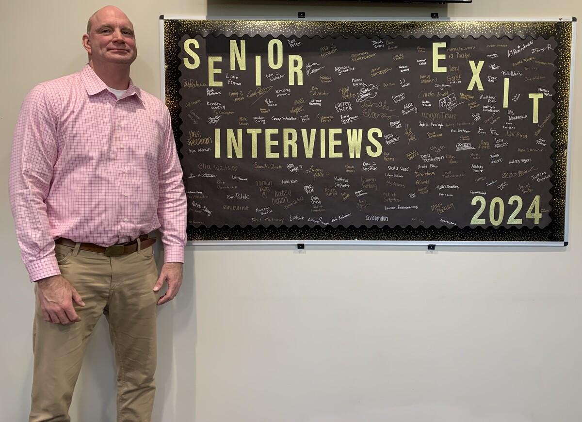 THS Principal Andy Jados poses next to the senior exit interview bulletin board