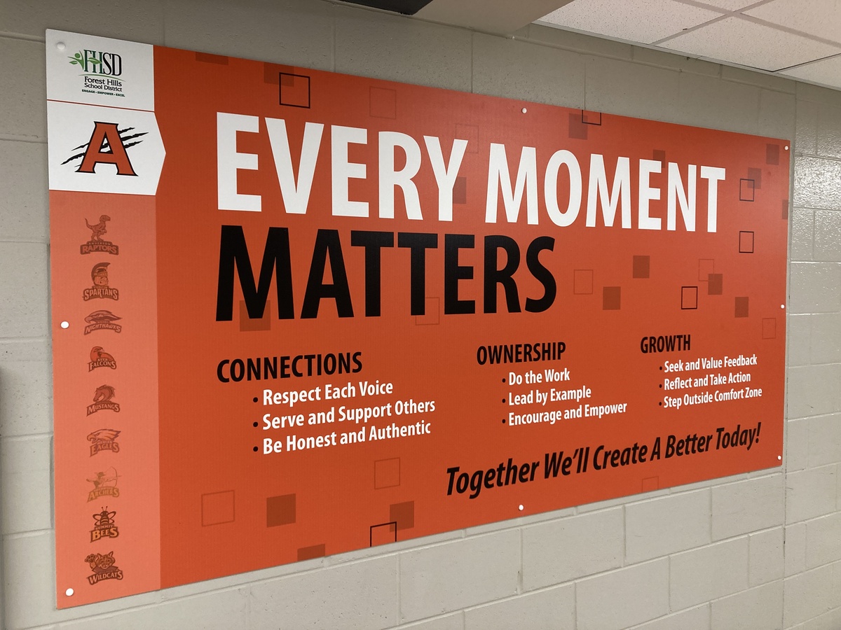 an orange sign on a school hallway reads "every moment matters, connections, ownership, growth"