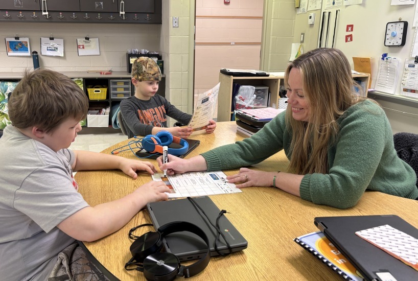 teachers smiles and points to a students paper to provide instruction
