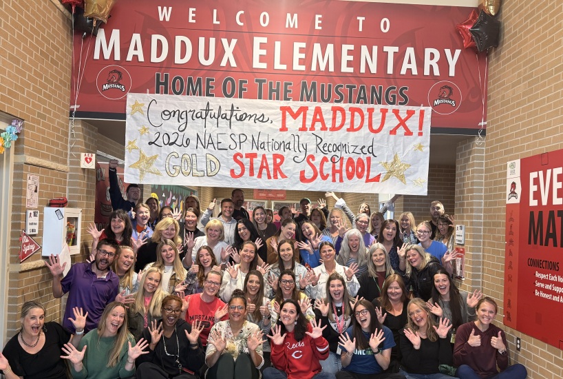 Maddux teachers and staff hold up their hands in front of a sign that says "congratulations, maddux! 2026 NAESP Nationall recognized Gold star school"